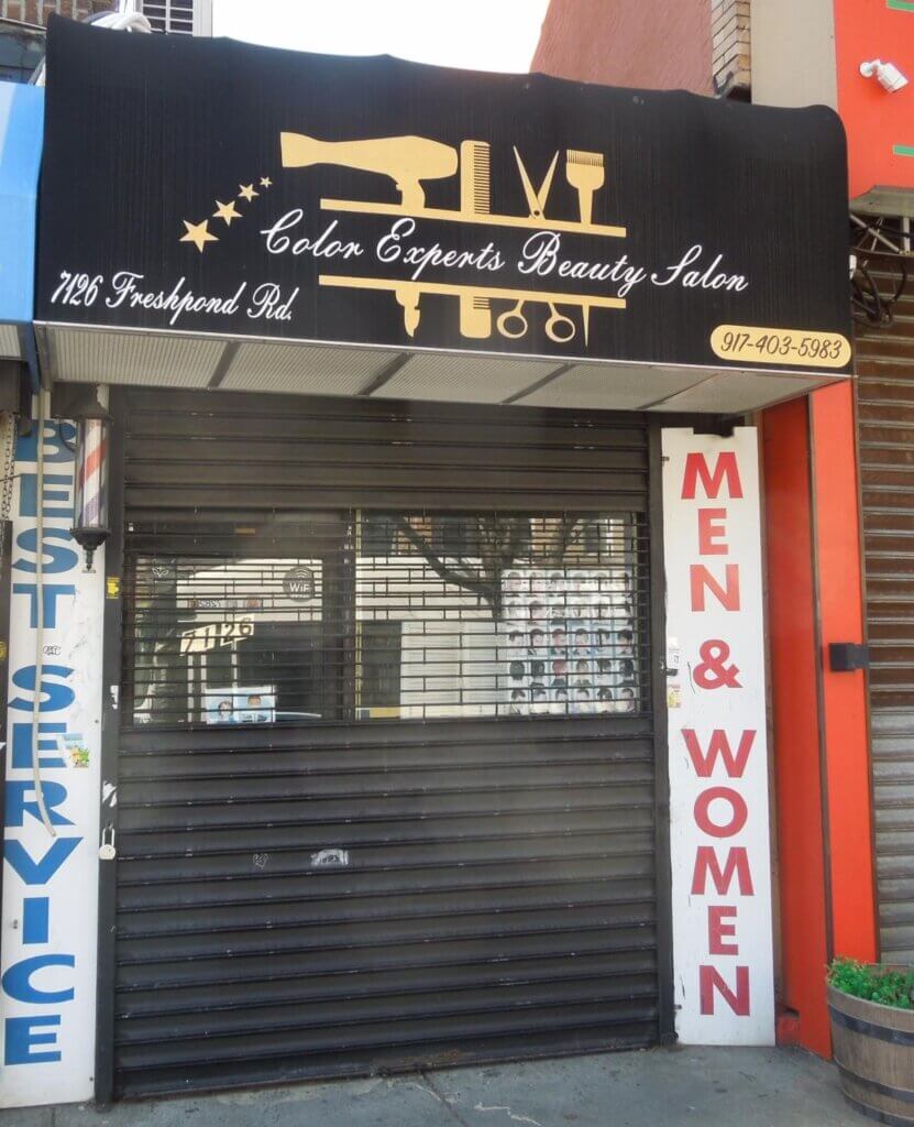 A closed beauty salon with a black awning displaying the name "Color Experts Beauty Salon" and its address, 1126 Freshpond Rd, along with a phone number. The entrance has a metal security shutter, and signs on either side read "BEST SERVICE" and "MEN & WOMEN.