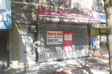 A storefront with a metal gate down and a red "Store for Rent" sign showing 1000 sq ft plus cellar, contact info, and a maroon awning for a dress shop. Brick building, tree shadow, and sidewalk visible.