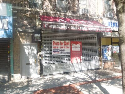 A storefront with a metal gate down and a red "Store for Rent" sign showing 1000 sq ft plus cellar, contact info, and a maroon awning for a dress shop. Brick building, tree shadow, and sidewalk visible.