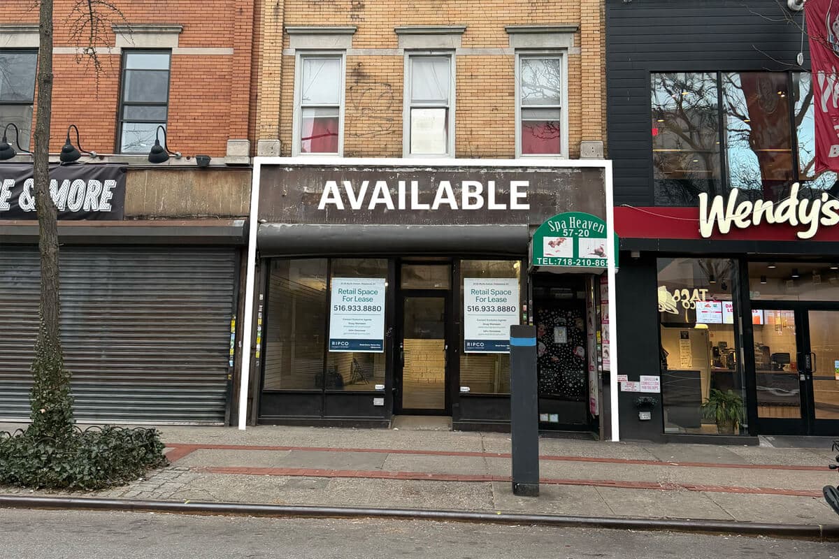A vacant retail storefront with a large "AVAILABLE" sign above it, flanked by neighboring businesses. The windows display contact information for leasing space. The street is empty, and a tree grows on the sidewalk.